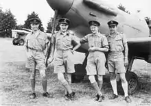 Four men wearing military uniforms posing in front of a propeller-driven aircraft