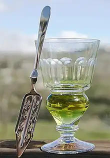 Image 27A reservoir glass filled with a naturally colored verte absinthe, next to an absinthe spoon (from List of alcoholic drinks)