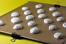 A metal sheet, lined with brown paper.  The paper is clipped to the side of the pan.  There are cookies on the paper, ready to bake.