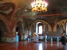 Side view of a narthex in an Eastern Orthodox temple. In the center is an analogion at which the priest hears confessions, to the right of that is a silver baptismal font and vessels for dispensing holy water. The main hall is to the left (Pechersky Ascension Monastery, Nizhny Novgorod).