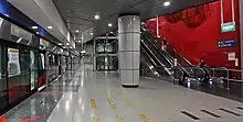 A train arrives at the CCL platform (on the left). The artwork of glass fins is on the red wall on the right, above the escalators.