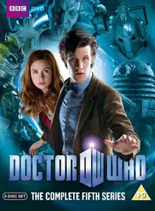 A DVD boxset cover consisting of a man with black hair reaching forward over a logo which says "Doctor Who". He is wearing a bowtie and tweed jacket. Looking out from behind him is young woman with red hair, wearing a red shirt and brown jacket. The background is blue and shows a masked reptilian humanoid, a statue with open jaws, the head of a robot, and a robot-like creature with an eyestalk.