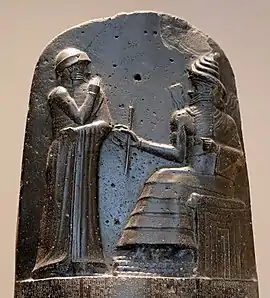 Hammurabi (standing), depicted as receiving his royal insignia from Shamash (or possibly Marduk). Hammurabi holds his hands over his mouth as a sign of prayer (relief on the upper part of the stele of Hammurabi's code of laws).