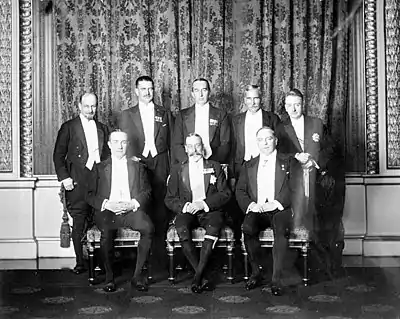 A group pose of eight men in smart evening wear. The King sits in the middle surrounded by his prime ministers.