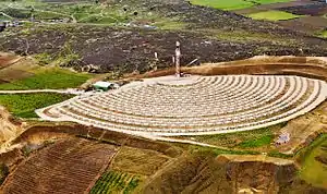 Distant view from a high point of a hill with concentric rows of mirrors most of the way around a slim tower