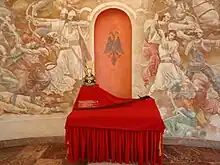 Mural commemorating a battle of Skanderbeg. The Arms of Skanderbeg visible in the forefront are copies of the originals held at the Art Museum of Vienna.