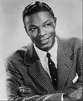 A black-and-white image of a man wearing a suit and looking towards the camera.