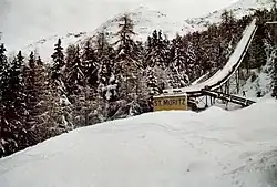 A snow-covered ski jump with the words, "St. Moritz" at the base