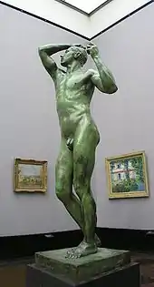 Life-sized nude stature of a male on a pedestal on display in a museum.