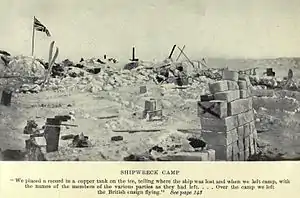 Boxes and equipment strewn around in disorderly piles on a broken ice surface. To the left a flag flies from a pole.