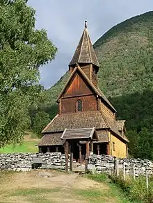 A small timber church in a courtyard surrounded by a stone fence